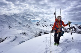 Caroline Gleich stands on top of a mountain with skis on her backpack.