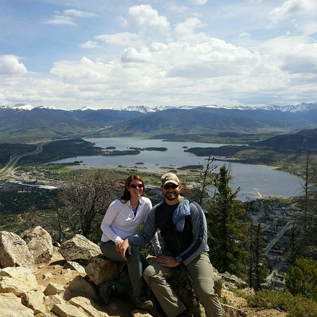 a couple posing at th etop of a hike with a city miles below