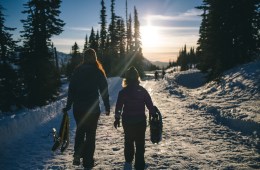 two women carrying snowshoes on a groomed winter trail