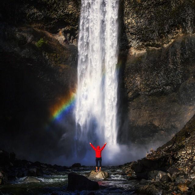 person holding their arms up high in front of waterfall