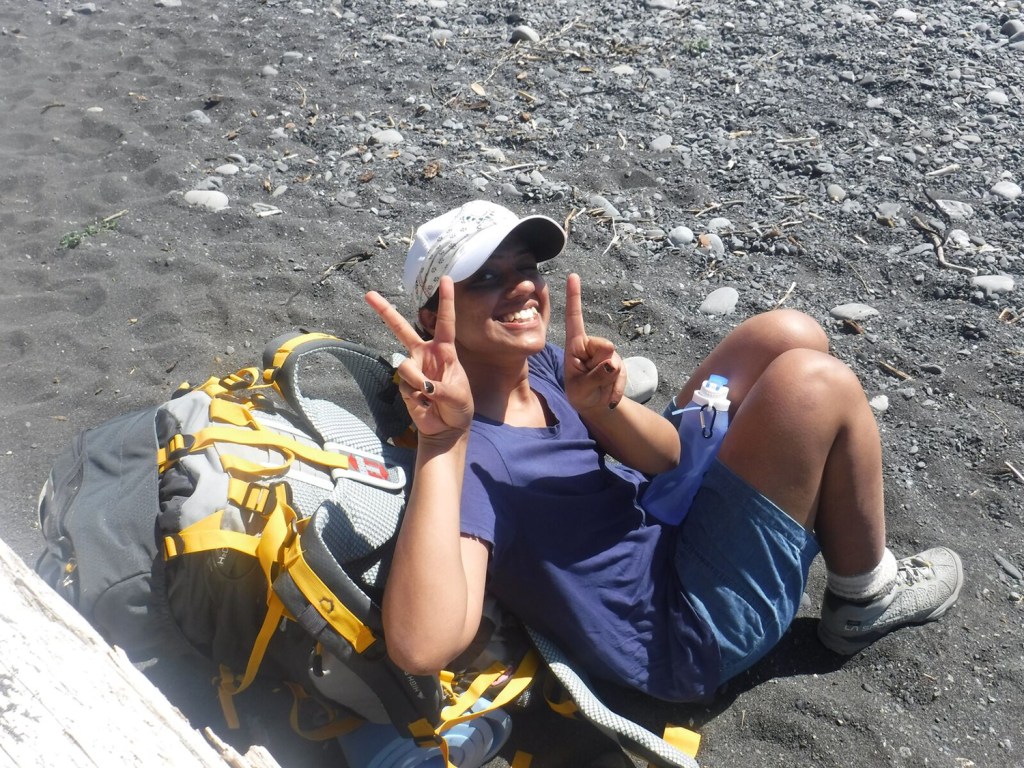 REI Adventures trip a hiker resting on a rocky and sandy beach.