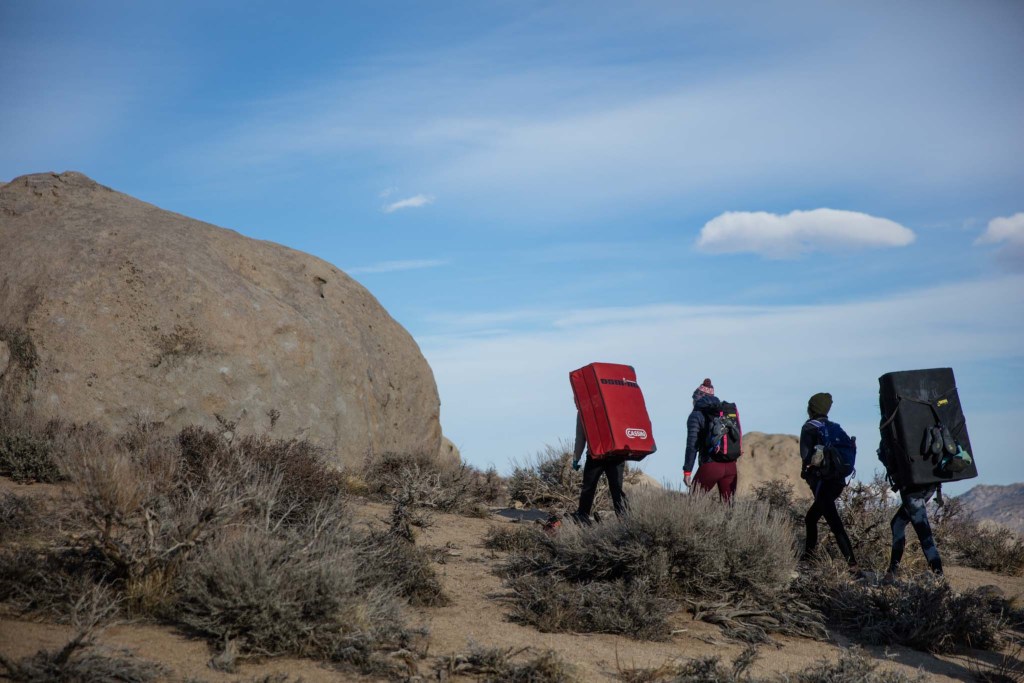 A group of women walking in the desert with bouldering pads to climb.