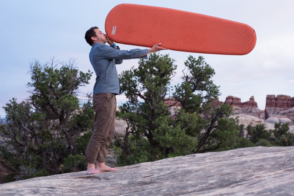 man blowing up sleeping pad at campsite