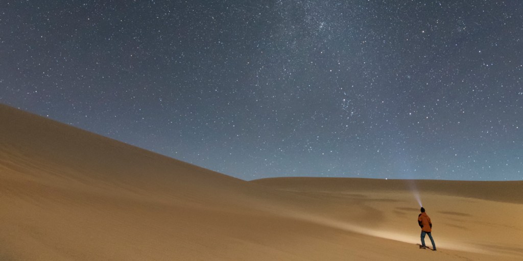 A hiker treks up a sand dune at night. 