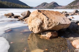 A rock in a body of shallow water in front of mountain peaks