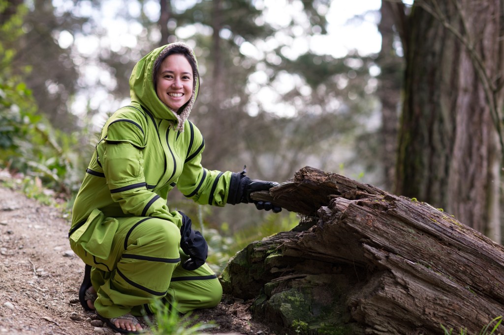Woman in Zipall suit crouched next to a log