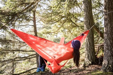 A person relaxes in a red hammock while reading.
