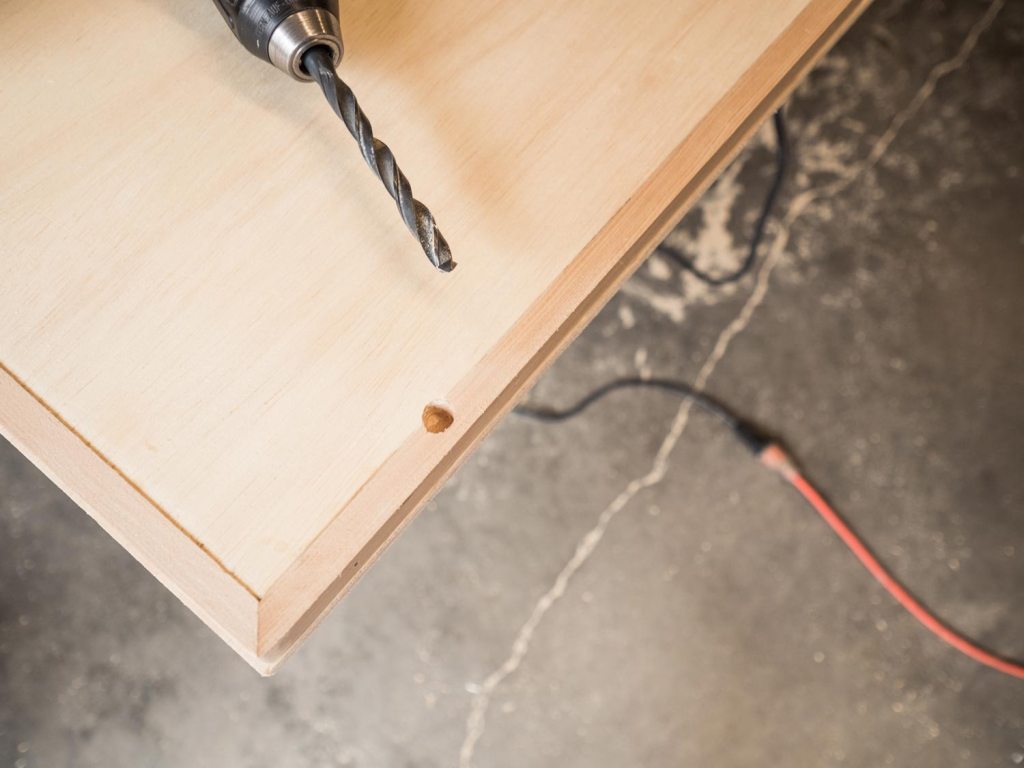 Person using the drill bit to make holes at the marks on the underside of the table