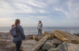 Two people standing on rocky outcrop looking out toward expansive ocean and sky.