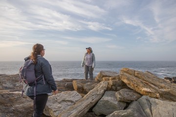 Two people standing on rocky outcrop looking out toward expansive ocean and sky.