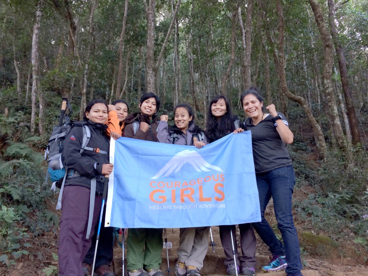 A group of girls in a forest holding a Courageous Girls flag.