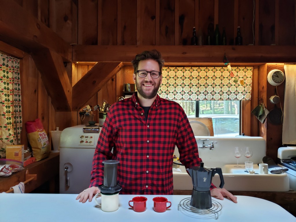 A man standing in the kitchen of a cabin with the fixings for coffee.