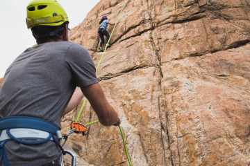 A rock climber wears a helmet while belaying another climber.