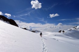 Lone thru hiker walks through snow with bright blue sky in the background.