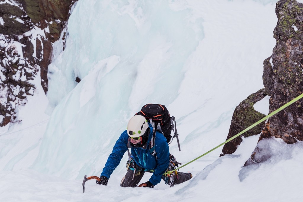 An ice climber reaches out, carefully placing his ice axe to pull himself up a frozen waterfall.