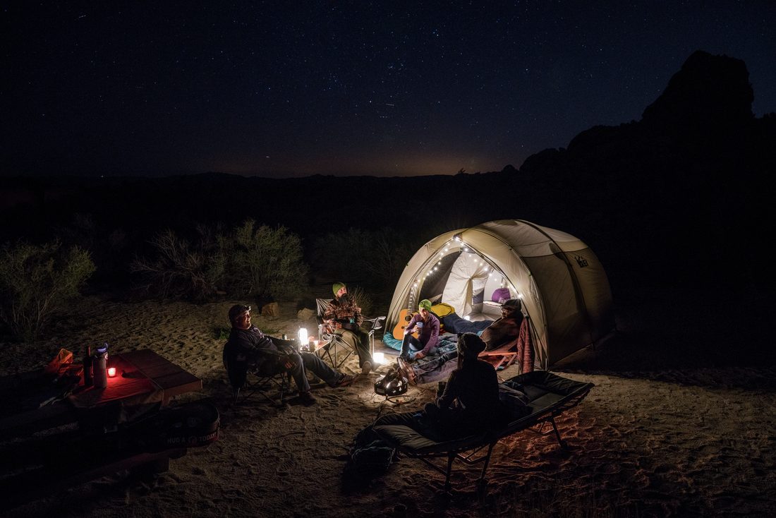 People sitting outside a tent with twinkle lights at night.