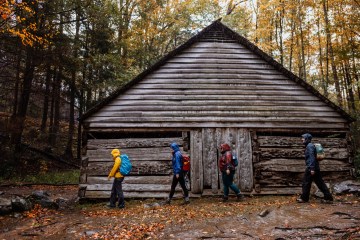 Hikers trudge by a wooden structure in Great Smoky Mountains National Park with the autumn leaves all around
