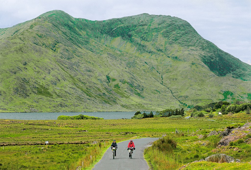 Cyclists navigate the green, pastoral landscape of the Irish countryside.