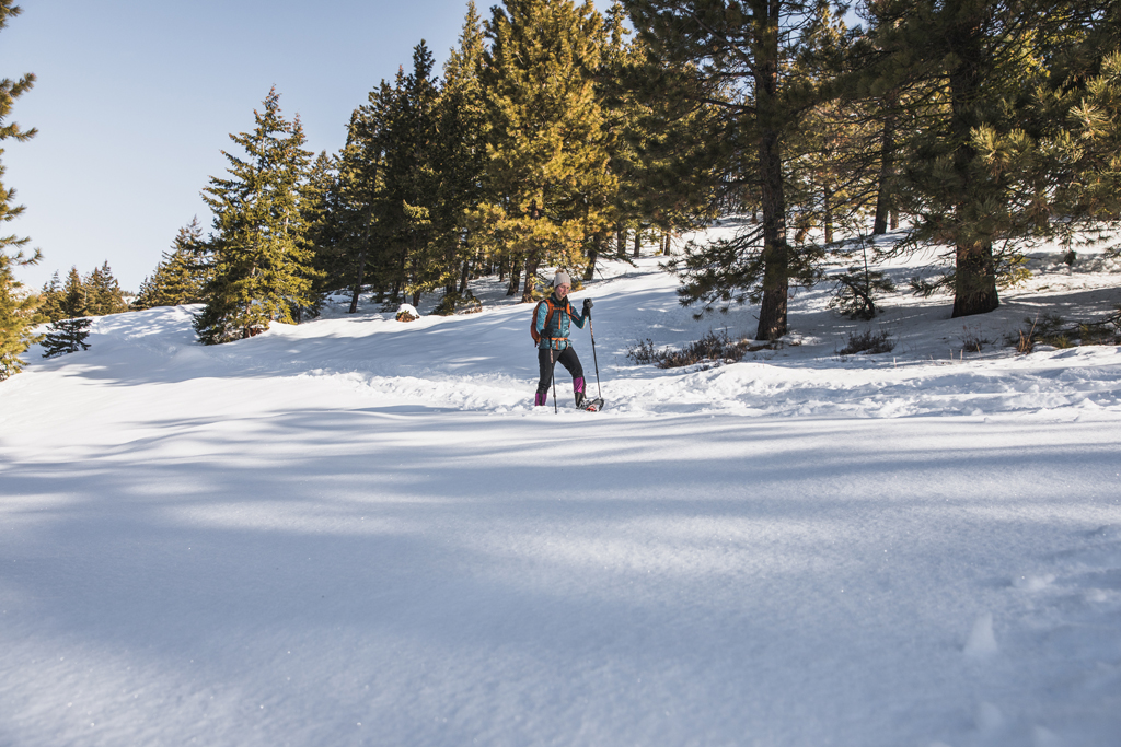 A woman crosses a snowy field in snowshoes