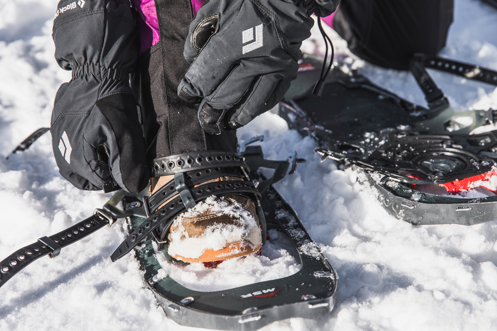 A woman adjusts the bindings of the MSR Lightning Ascent women's snowshoes