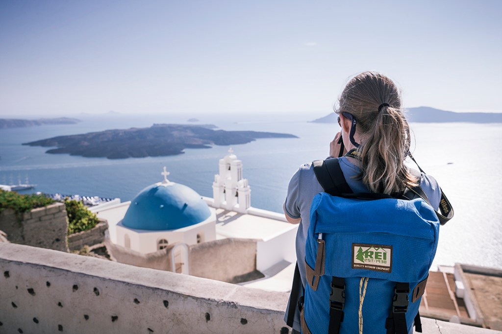 A hiker overlooks the island-filled sea below Santorini.