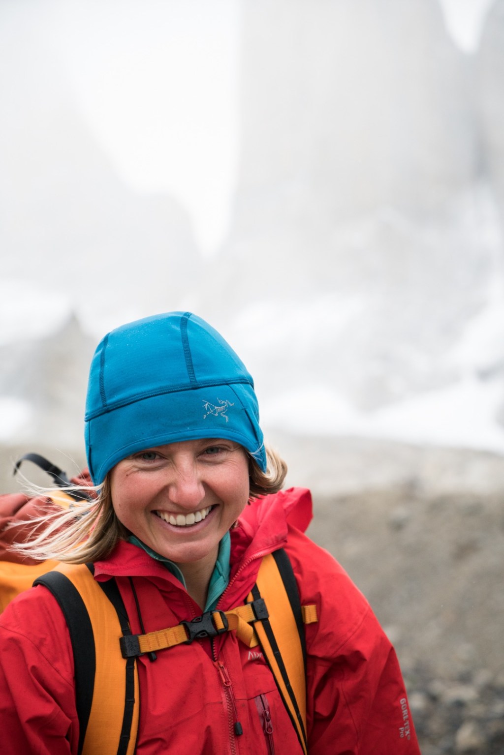 Brette Harrington smiles, wearing a warm hat, jacket and backpack, with rock spires rising from the backround behind her.