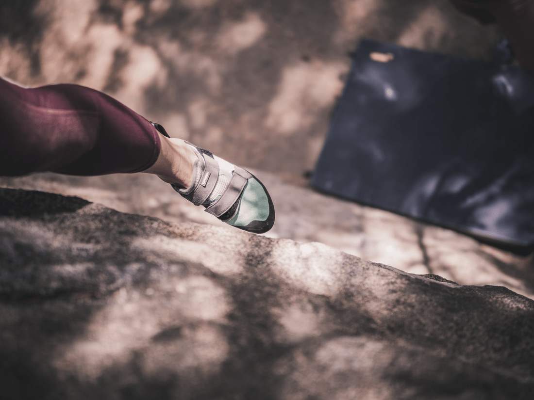 A climber's foot flags above a bouldering pad.