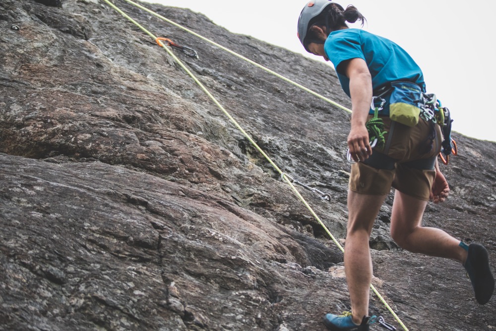 A rock climber wearing a helmet lowers down a rock wall.