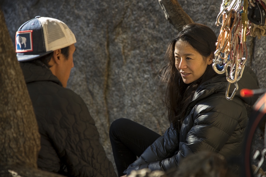 Jimmy Chin and Chai Vasarhelyi have a conversation amongst climbing gear, sitting against a cliff face.