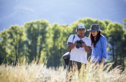 Two filmmakers stand in a sunny field to look at a shot recently captured on their camera