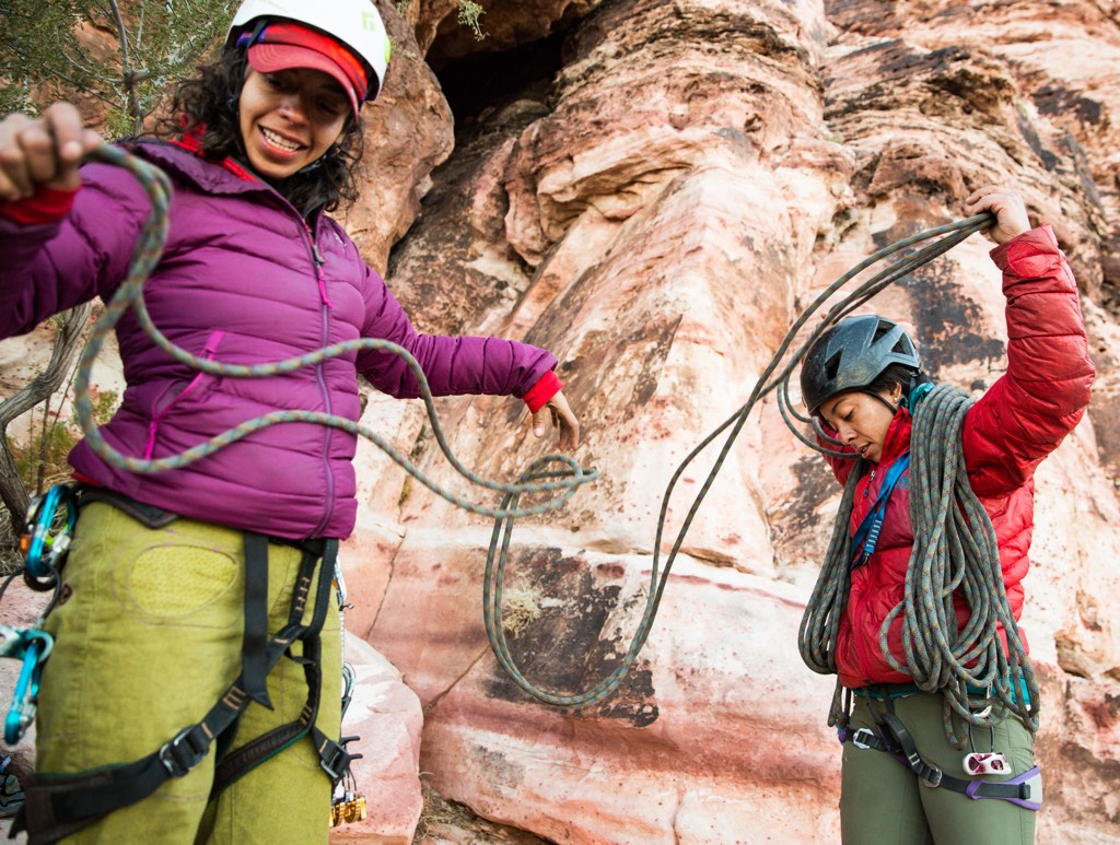 Two women in climbing helmets, harnesses and jackets sort and coil a climbing rope.