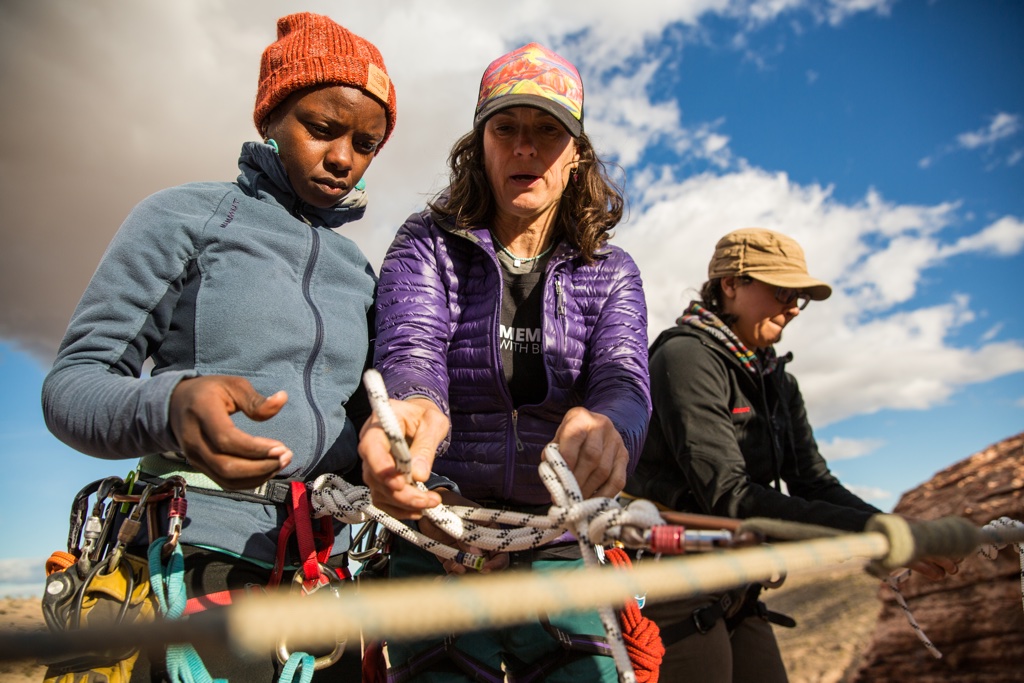 One woman shows another how to tie a knot with a climbing rope.