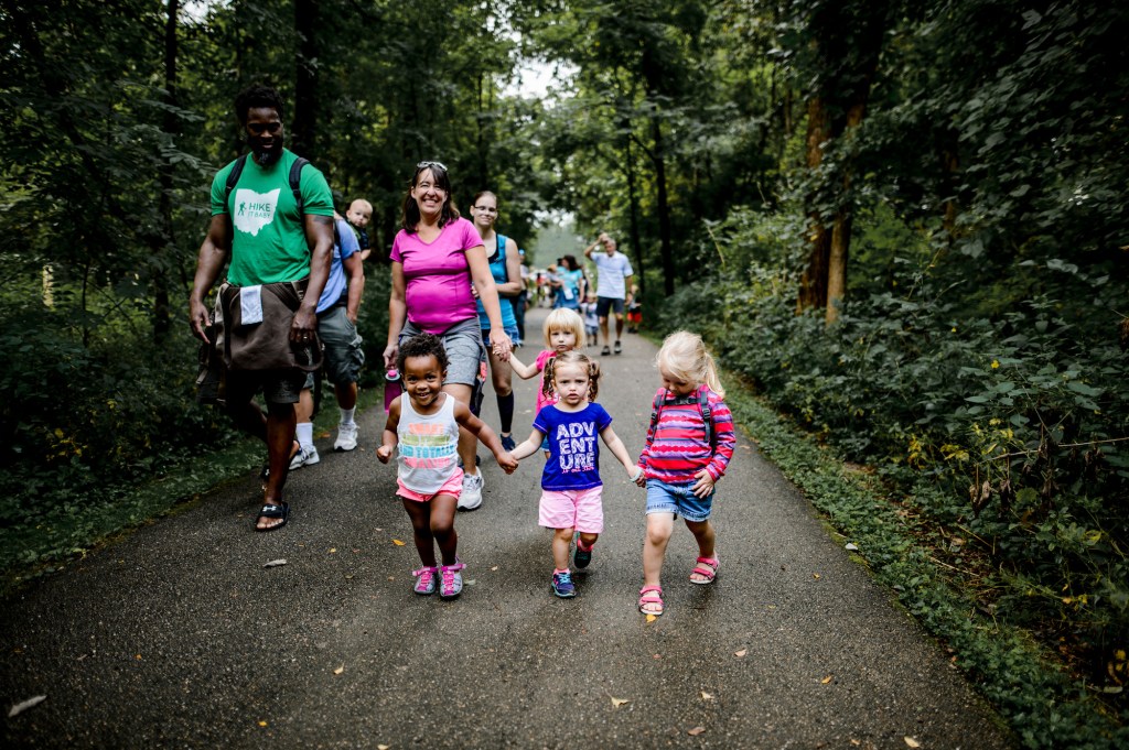 A group of children and caregivers walk on a wide path through a forest