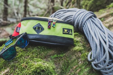 Sunglasses, waistpack and climbing rope lay on a mossy log.