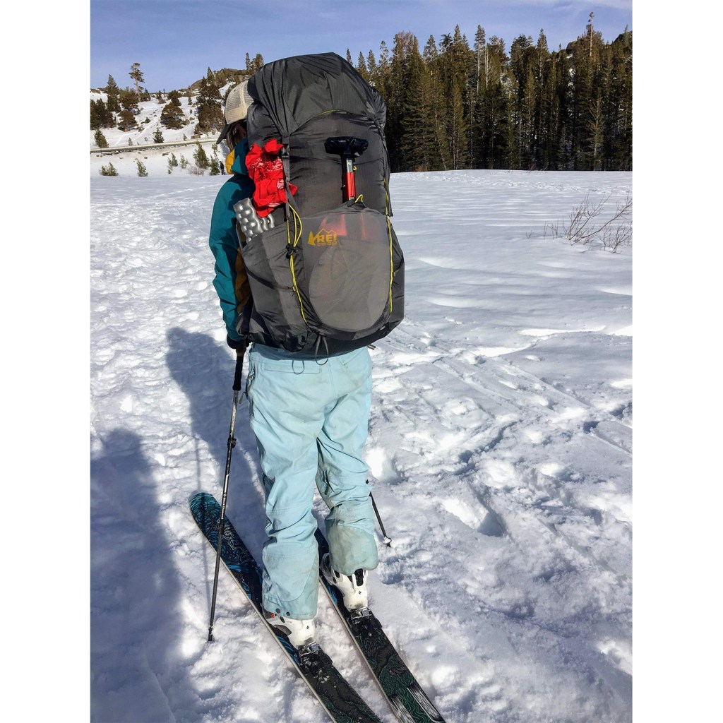 A close-up shot of a backpacking pack weighed down with gear on the back of a woman in the snow