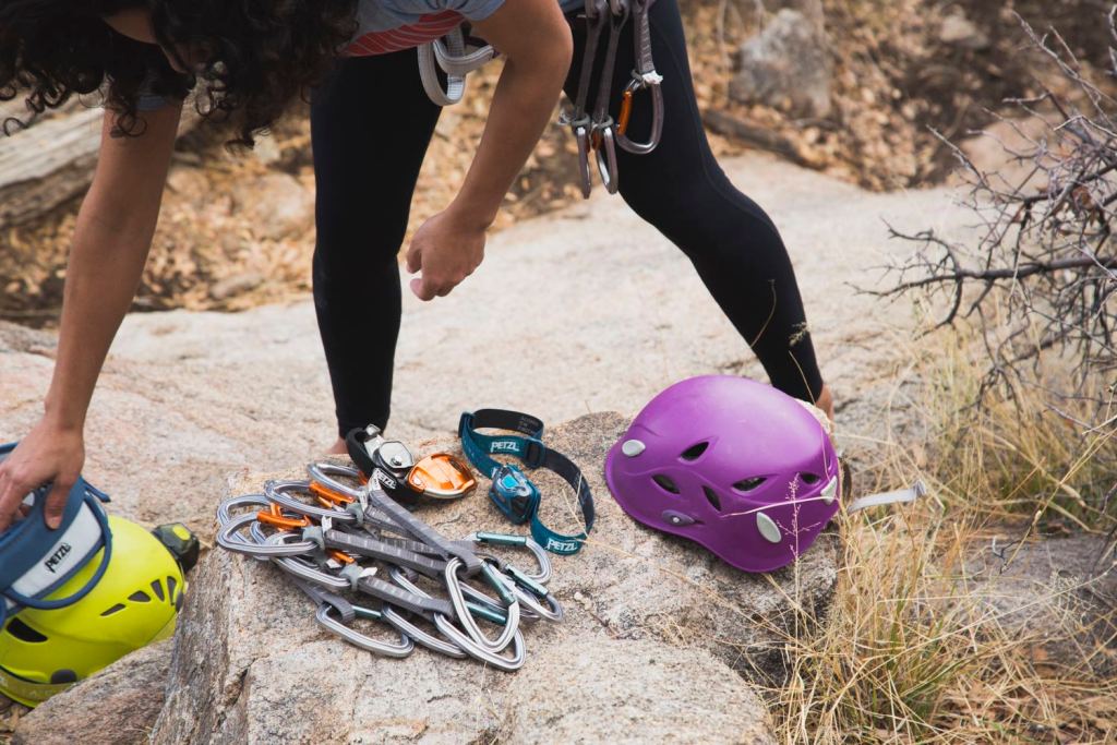 A rock climber arranges quickdraws, a headlamp, helmet and other gear on a rock.