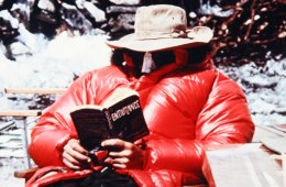 A rock climber on the 1963 American Mount Everest Expedition lounges in a big, red puffy jacket, reading the book "Endurance."