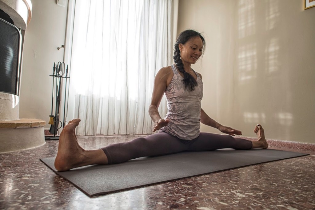 Olivia Hsu sits on a yoga mat with her legs stretched out in Side Splits pose.