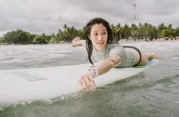 A woman paddles out into calm surf.