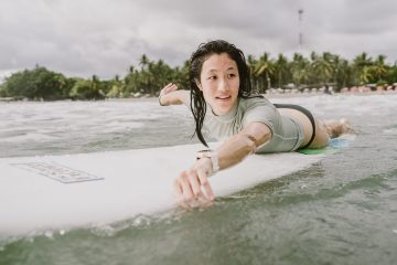 A woman paddles out into calm surf.
