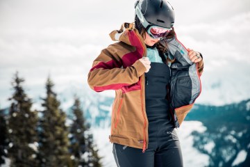 A skier zips up her jacket over a pair of bib pants.