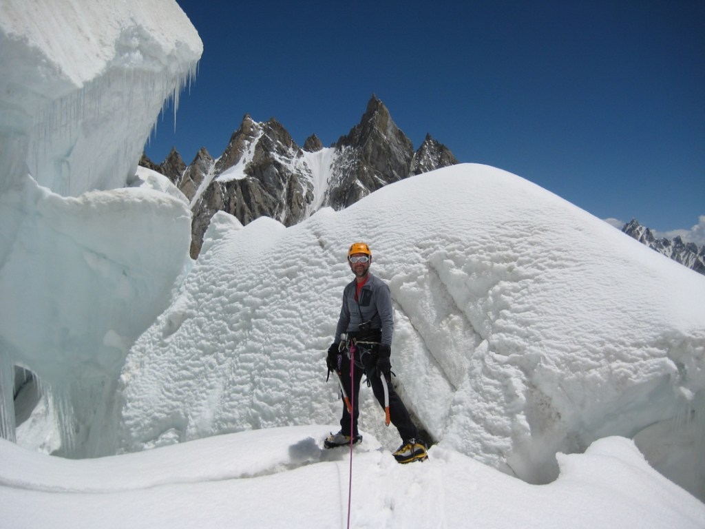 Steve Swenson stands in alpine climbing gear in front of a human-height ice formation on Latok I.