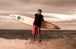 Brian Keaulana with a surf board standing on the beach.