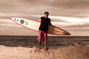 Brian Keaulana with a surf board standing on the beach.