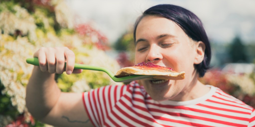 The writer takes a big bite out of a pancake with jelly on top from the spatula.