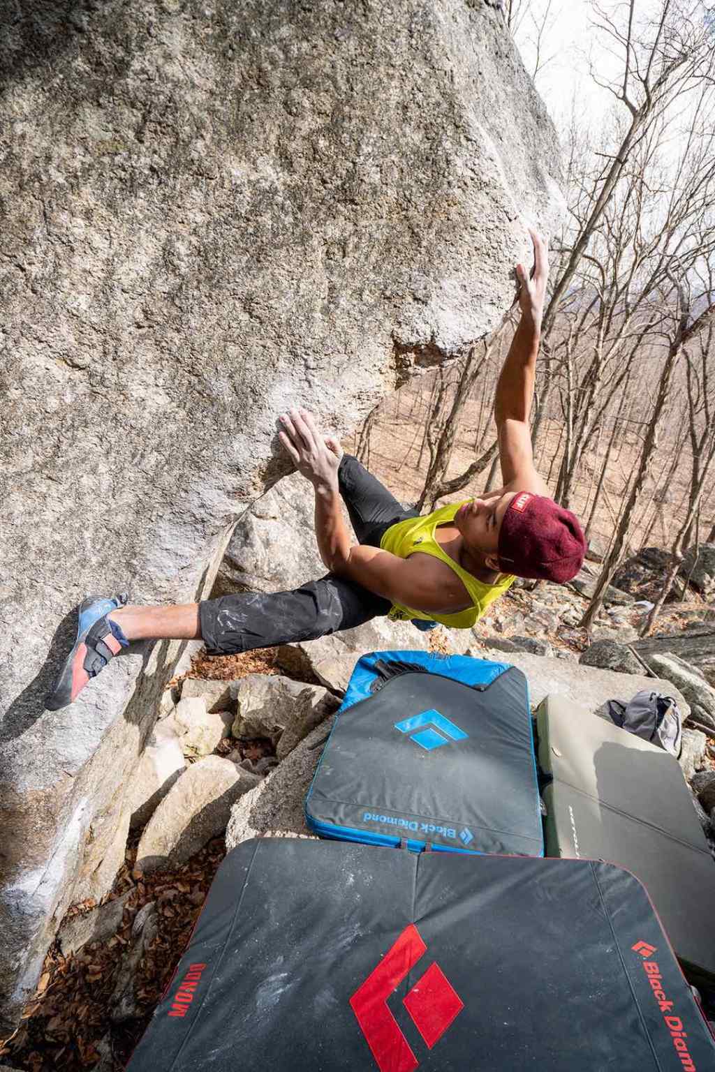 Kai Lightner uses his left foot to heel hook while climbing a boulder outdoors.