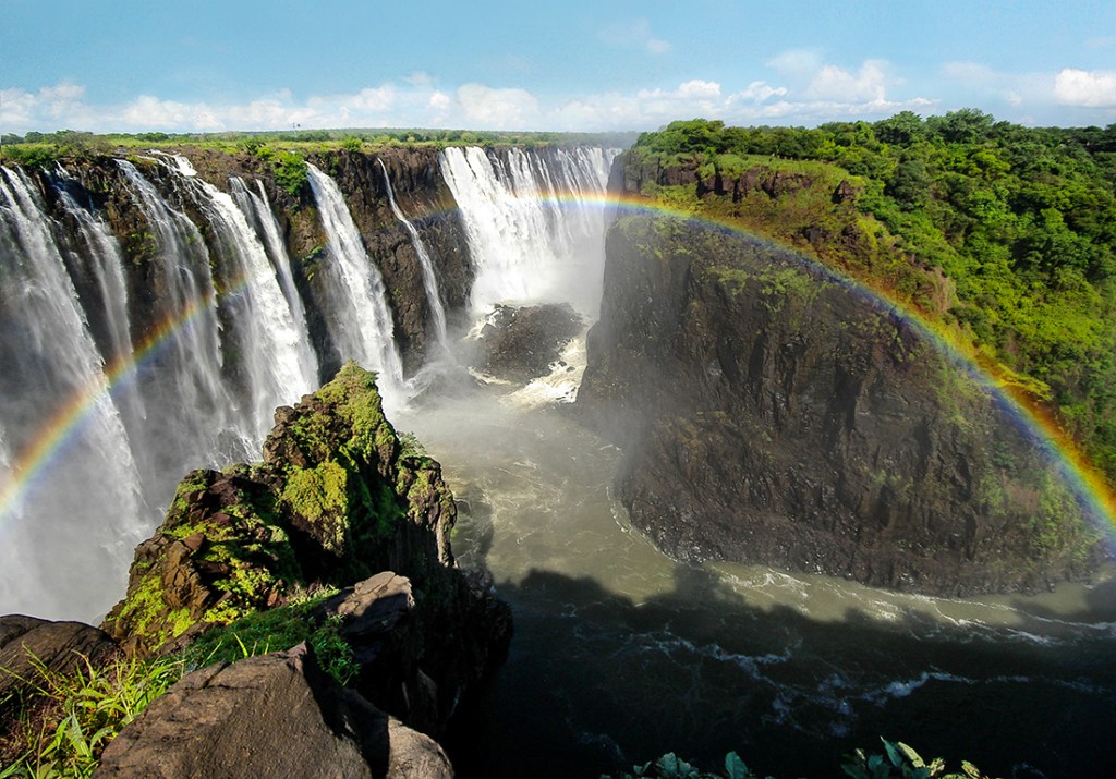 A rainbow shines over a misty Victoria Falls.