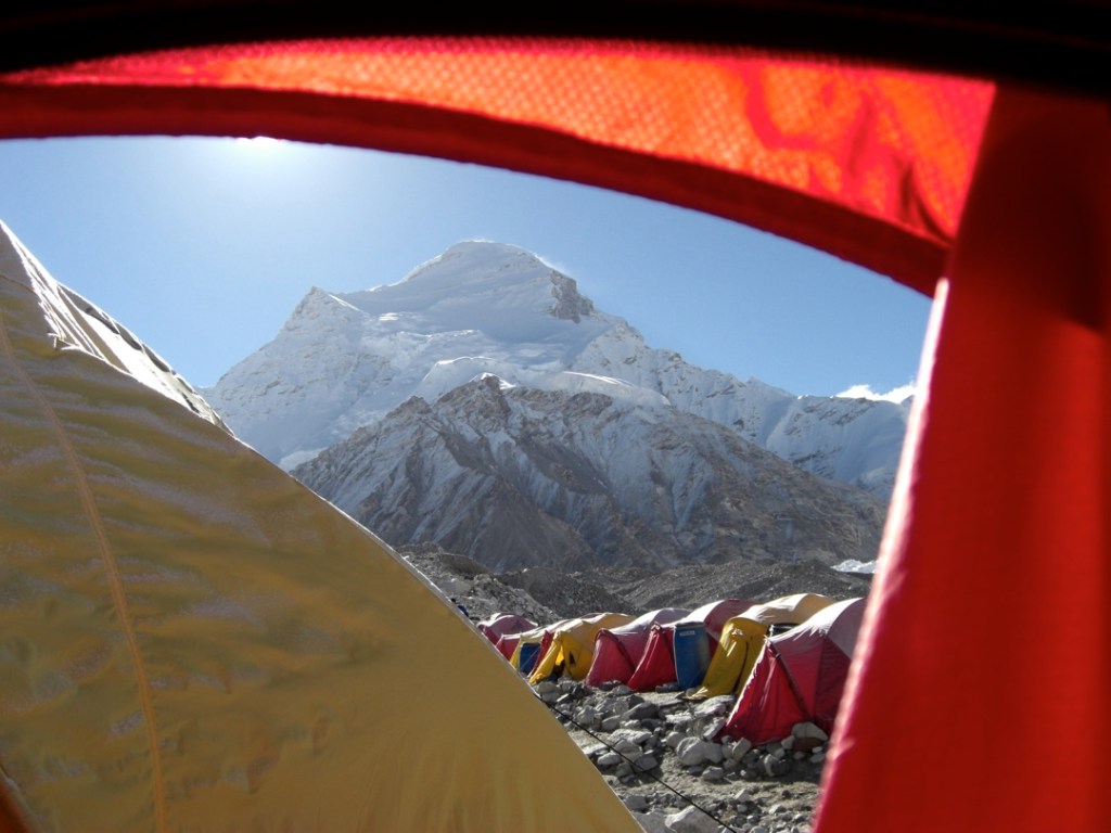 Brightly colored tents stand in a neat row in front of a snowy peak. 