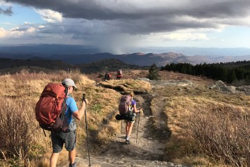 Hikers traverse a high-alpine field under stormy skies