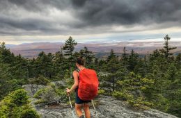 Heather Anderson walks with a heavy pack across a bald mountain with stormy skies in the distance